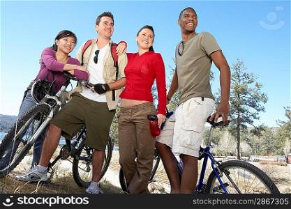 Four young adults standing by lake shore with mountain bikes.