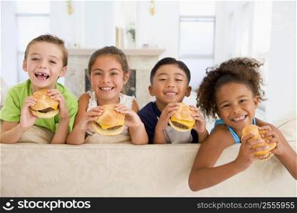 Four young children eating cheeseburgers in living room smiling