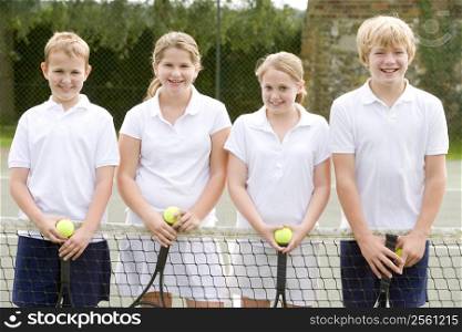 Four young friends with rackets on tennis court smiling