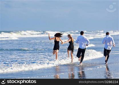 Four young people, two couples, having fun and running into the sea on a beach