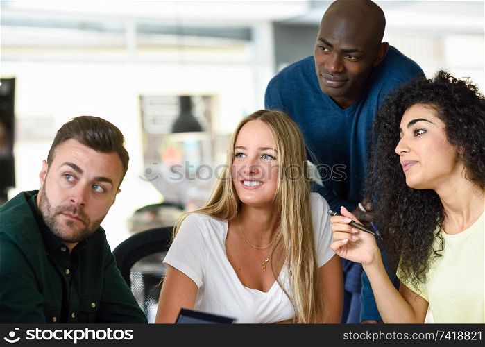 Four young people working together. Beautiful men and women in a business meeting wearing casual clothes. Multi-ethnic group.. Beautiful men and women working toghether wearing casual clothes.