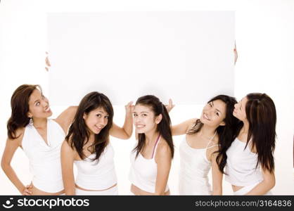 Four young women and a teenage girl holding a blank placard and smiling