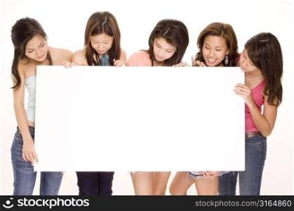 Four young women and a teenage girl looking at a blank placard and smiling