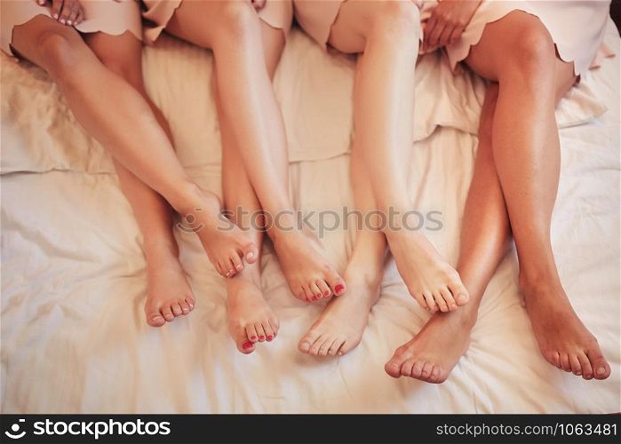 four young women lying on the bed with bare legs. Women in sleeping robe lying in bedroom. legs of girlfriends of the bride