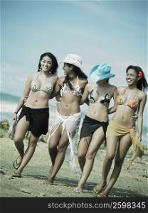 Four young women standing with their arms around each other walking on the beach