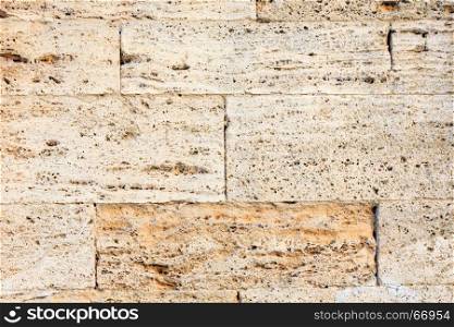 Fragment of a stone wall made of limestone bricks with spongy surface (architectural background pattern).