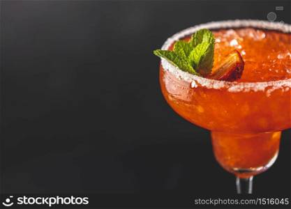 Fragment of frozen strawberry lime mint margarita in tall footed glass on the dark background close up. Luxury alcohol fresh