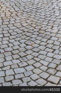 Fragment of old gray cobblestone road with dry leaves
