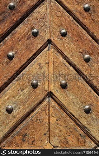Fragment of old vintage wooden doors with metal rivets, close-up architectural texture