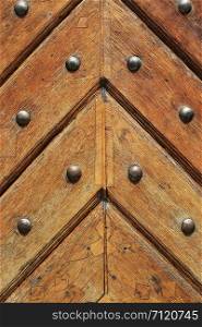 Fragment of old vintage wooden doors with metal rivets, close-up architectural texture