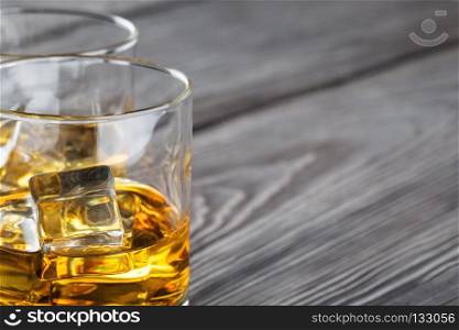 Fragment of two glasses of whiskey with ice on wooden background blurred. Fragment of two glasses of whiskey with ice
