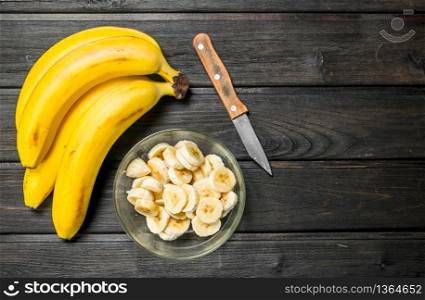 Fragrant bananas and banana slices in a glass bowl with a knife. On a black wooden background.. Fragrant bananas and banana slices in a glass bowl with a knife.