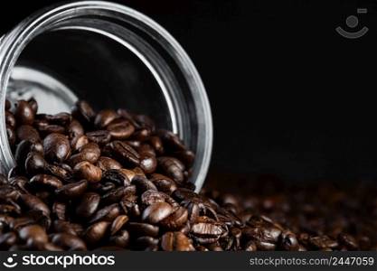 Fragrant coffee beans are scattered from a jar on a rustic tabletop background. Close-up, selective focus. Copy space banner.