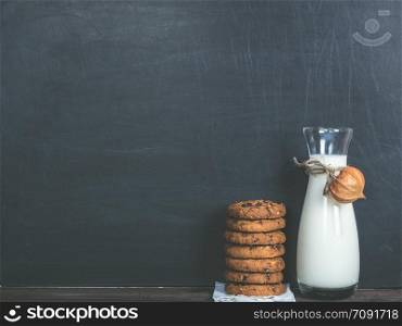 Fragrant cookies with chunks of chocolate and a jug of fresh milk on a black background. Fragrant cookies and fresh milk