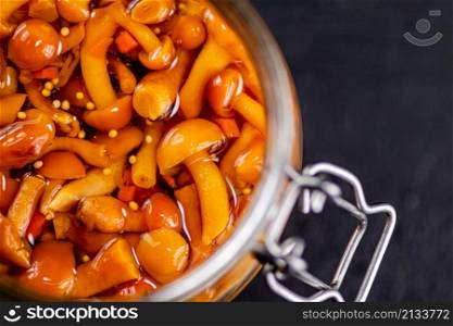 Fragrant pickled mushrooms in a glass jar. On a black background. High quality photo. Fragrant pickled mushrooms in a glass jar.