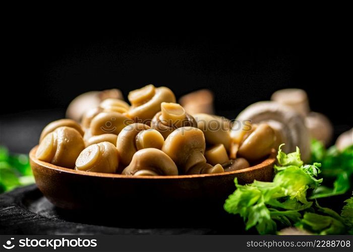 Fragrant pickled mushrooms in a plate with greens. On a black background. High quality photo. Fragrant pickled mushrooms in a plate with greens.
