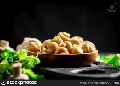 Fragrant pickled mushrooms in a plate with greens. On a black background. High quality photo. Fragrant pickled mushrooms in a plate with greens.