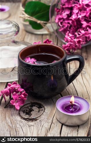 fragrant spring flower tea on the background of burning candles and lilac bouquet. fragrant tea and a branch of lilac