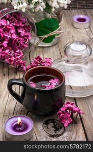 fragrant spring flower tea on the background of burning candles and lilac bouquet. fragrant tea and a branch of lilac