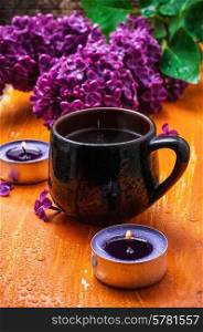 fragrant spring flower tea on the background of burning candles and lilac bouquet. flower tea