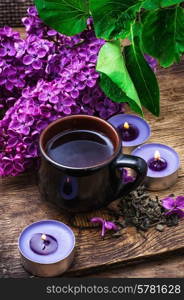 fragrant spring flower tea on the background of burning candles and lilac bouquet. flower tea