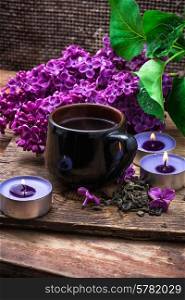 fragrant spring flower tea on the background of burning candles and lilac bouquet. flower tea