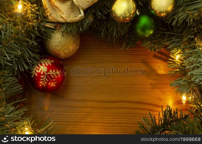 Frame formed by green Christmas tree branches, yellow lights, golden and red light bulbs on a wooden table. Frame made up of Christmas tree branches, yellow lights, golden and red light bulbs on a wooden table
