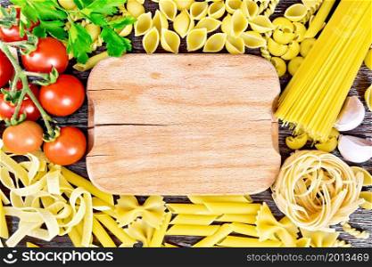 Frame from a wooden plate, different pasta, tomatoes, garlic and parsley on a wooden board background