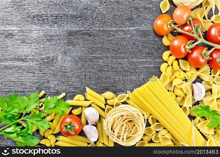 Frame made of different pasta, tomatoes, garlic and parsley on a black wooden board background