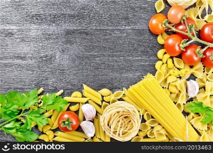 Frame made of different pasta, tomatoes, garlic and parsley on a black wooden board background