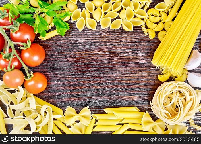 Frame made of different pasta, tomatoes, garlic and parsley on a brown wooden board background