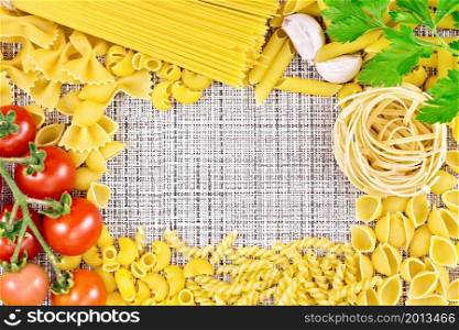 Frame made of different pasta, tomatoes, garlic and parsley on the background of a coarse wicker fabric