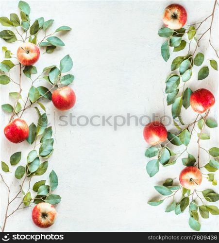 Frame made with red apples and green branches with leaves on white desk background. Top view. Flat lay. Border of apples. Food layout background