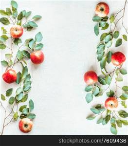 Frame made with red apples and green branches with leaves on white desk background. Top view. Flat lay. Border of apples. Food layout background