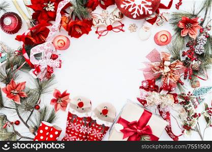 Frame made with red Christmas decoration, funny deer socks and gift box on white background with fir branches and candles. Top view. Christmas background. Flat lay