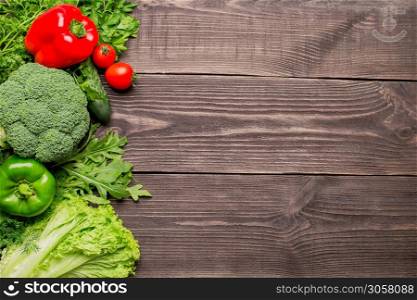 Frame of green fresh vegetables on wooden background, top view. Pepper, broccoli, lettuce, cucumber, arugula, parsley and tomatoes. Frame of green and red fresh vegetables on wooden background, top view