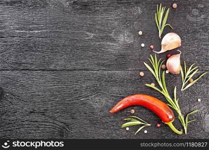 Frame of peas of colored pepper, fresh rosemary, pod of red hot pepper and two cloves of garlic on a black wooden board top