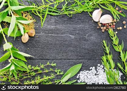 Frame of savory leaves, tarragon, sage and thyme, salt, nutmeg, mustard seeds, pepper and garlic on the background of wooden boards. Frame from herbs and garlic on black board