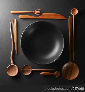 frame of setting empty black plate and wooden spoon, fork, knife on a black table.. frame of setting empty plate and wooden cutlery