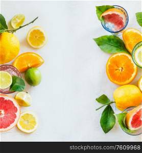 Frame of various citrus fruits with green leaves on white table, top view. Healthy lifestyle. Ingredients. Vitamin. Halves and slices. Layout