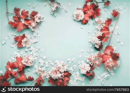 Frame of white flowers with red leaves on light blue background, top view. Frame. Copy space