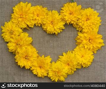 Frame of yellow flowers in the form of heart against a background of rough cloth