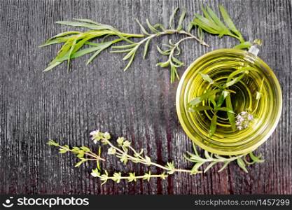 Frame with herbal tea in a glass cup, sprigs of tarragon, rosemary and thyme on wooden board background from above