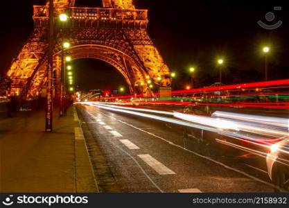 France, Paris. Traffic on the Jena bridge. Night at the foot of the Eiffel Tower. Many light trails from car headlights. Many Lights of Night Traffic on the Jena Bridge and Eiffel Tower