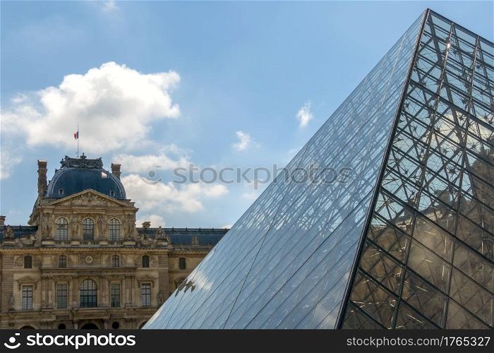 France. Sunny day in the Parisian courtyard of the Louvre Museum. Old facade and modern glass pyramid. Facade of the Louvre Museum and the Glass Pyramid