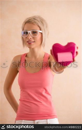 Freaky blond girl with short hair wearing glasses holding plastic heart and looking at camera. Valentine's day celebration