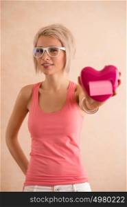 Freaky blond girl with short hair wearing glasses holding plastic heart and looking at camera. Valentine's day celebration