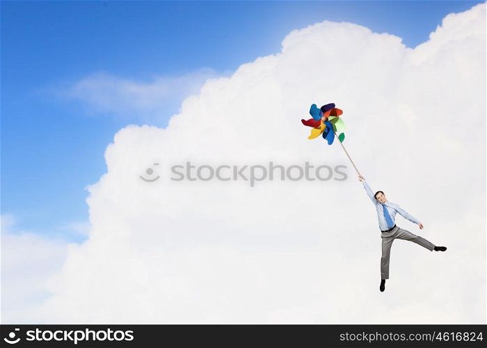 Free and careless. Young happy businessman flying in sky on colorful windmill