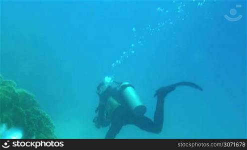 Free diver with aqualung and camera swimming underwater near the coral reef. Undersea shooting