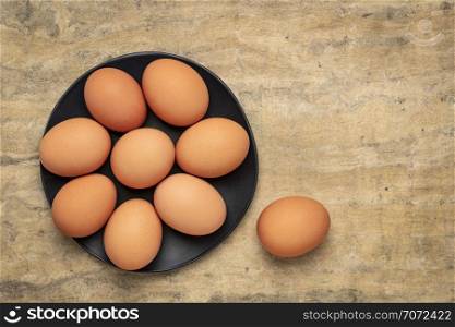 free-range large brown chicken eggs on a black plate against textured bark paper with a copy space
